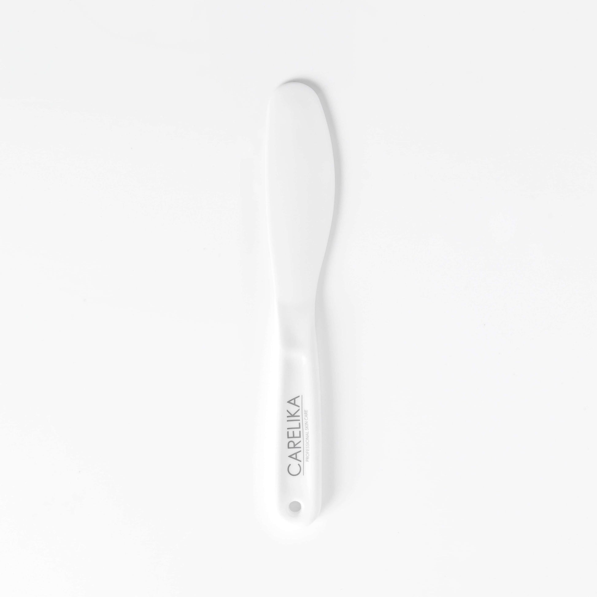 Carelika white silicone spatula for hygienic and even application of face masks in skincare routines.