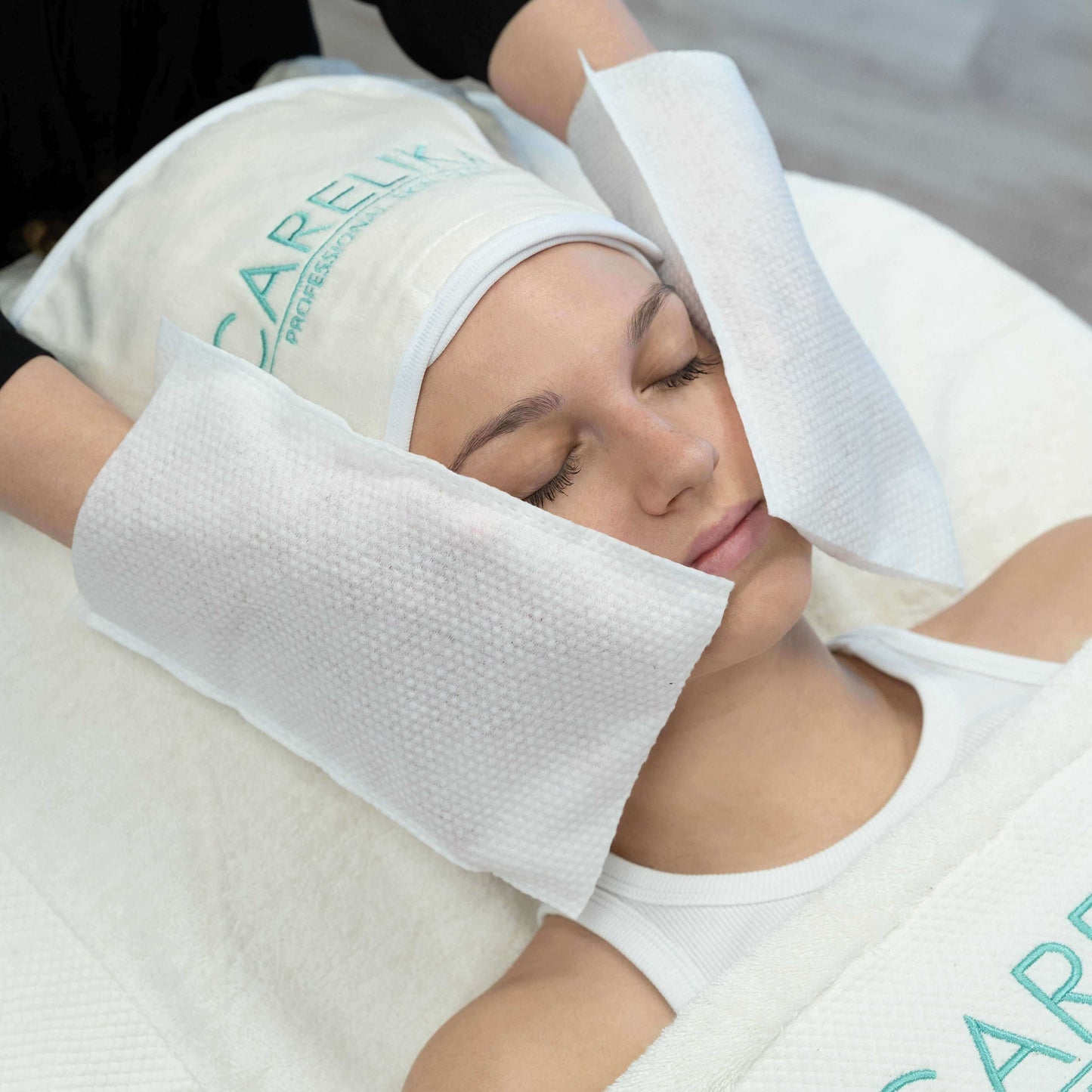 Woman receiving a soothing facial treatment with Carelika disposable soft wash mittens for cosmetologic procedures.